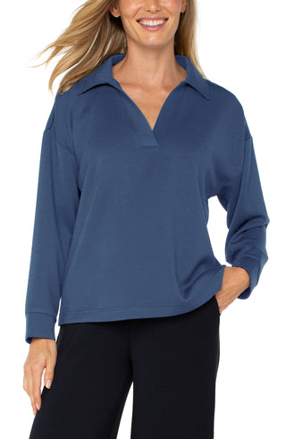 A woman wearing a blue V-neck popover with long sleeves and a collar.