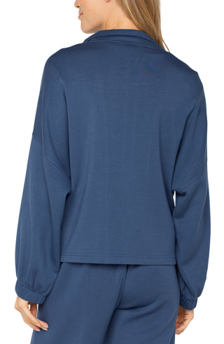 A woman wearing a blue zip up funnel neck jacket with a white top and blue trousers.
