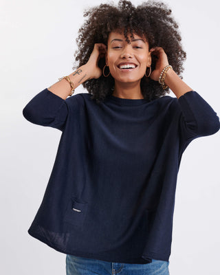 Woman wearing a navy blue sweater and blue jeans on a white background. Mersea Catalina Crewneck Sweater in Navy