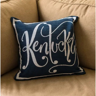 A navy throw pillow with the word 'Kentucky' written in a white script font, placed on a beige sofa cushion. Navy Kentucky Word Pillow