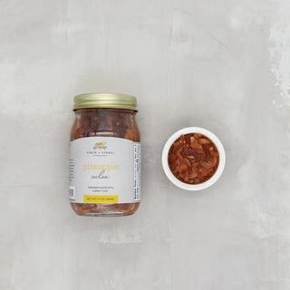 A jar of pineapple salsa next to a small white container of the salsa dipping sauce. Both are on a light background, finch and fennel 