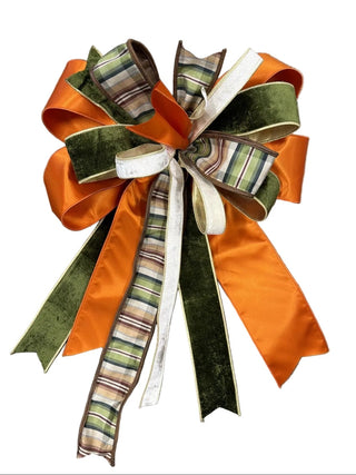 Plaid with Green, Orange and Brown Bow
A large autumn-themed decorative bow made from orange satin ribbons, olive green velvet ribbon, and plaid patterned ribbon, displayed on a dark wood floor.
