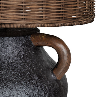 Close-up of a textured black pot with a wicker lid and metal handle on a white background