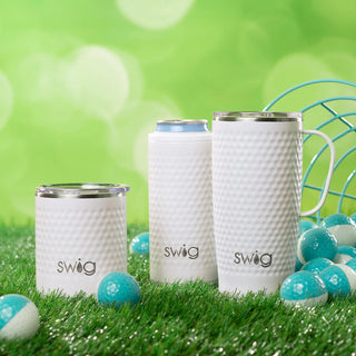 A white golf ball-textured can cooler with a SWIG logo, designed to keep beverages cold and hot next to a SWIG mug and cup