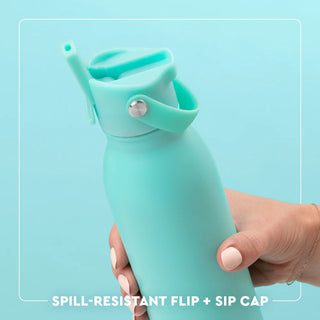 Turquoise water bottle with spill-resistant flip and sip cap held by a hand on a light blue background