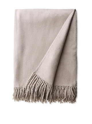 A folded silk fleece throw blanket in a stone color with a fringe, displayed on a flat surface.
