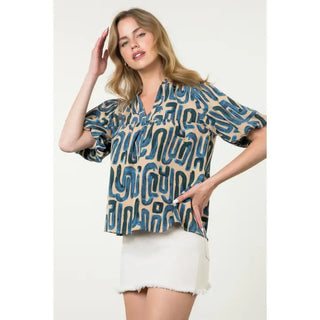 Woman wearing a THML blue and beige patterned top and white skirt on a plain background