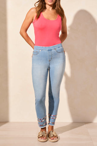 A pair of slim ankle jeans with embroidery on the lower legs, a mid-rise waist, and a pull-on waistband. The jeans are displayed on a person wearing a pink top.