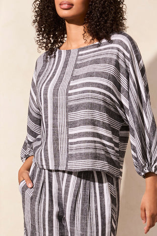 A woman wearing a black and white striped tribal boat neck blouse with dolman sleeves.