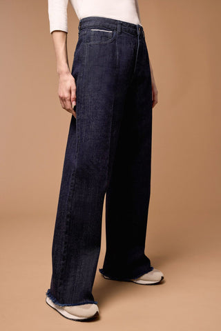 A person wearing Tribal Brooke Hugging Wide Trouser Jeans in a dark rinse color, with a high-rise waist and wide leg design, paired with a white top and beige shoes.