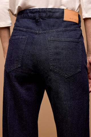 A person wearing Tribal Brooke Hugging Wide Trouser Jeans in a dark rinse color, with a high-rise waist and wide leg design, paired with a white top and beige shoes.