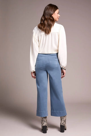 Woman wearing a white blouse and blue jeans against a plain background