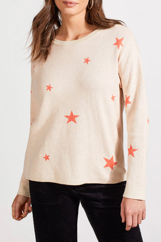 A woman wearing a beige and orange star-patterned crew neck reversible sweater