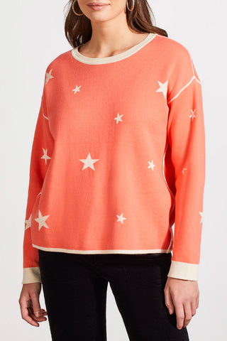 A woman wearing a beige and orange star-patterned crew neck reversible sweater