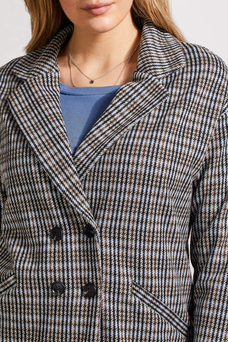 A woman wearing a double-breasted plaid blazer with a notch collar, in a blue and beige check pattern, paired with a blue top and jeans.