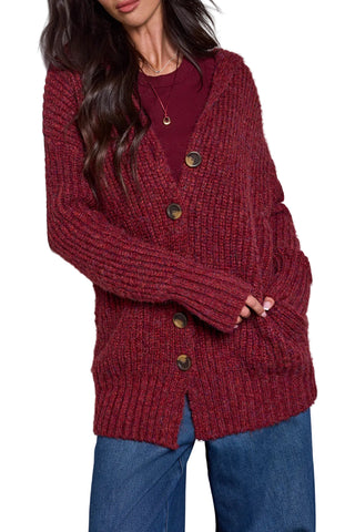 A woman wearing a chunky, ribbed knit cardigan in a deep burgundy red. The cardigan features a V-neck, front button closure with dark brown buttons, and side pockets. Tribal Long Oversized Cardigan Sweater in Heathered Pinot