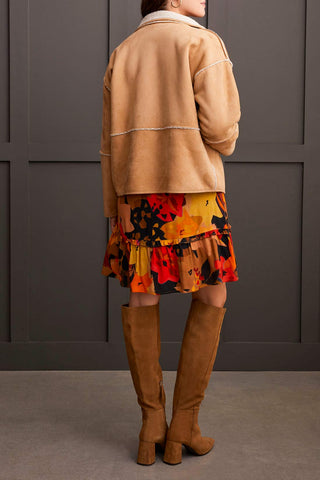 A woman wearing a beige long sleeve snap front reversible sherpa coat with a multicolored dress and brown boots.