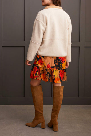 A woman wearing a beige long sleeve snap front reversible sherpa coat with a multicolored dress and brown boots.