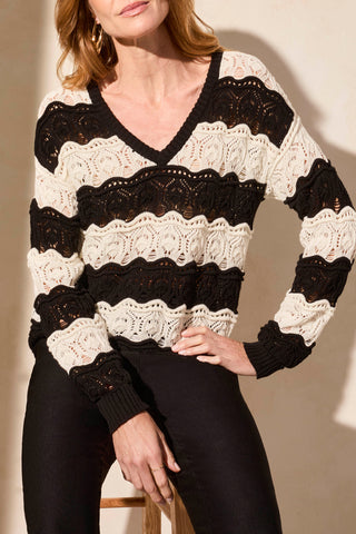 A woman wearing a long sleeve V-neck crochet swirl stripe sweater in black and cream.