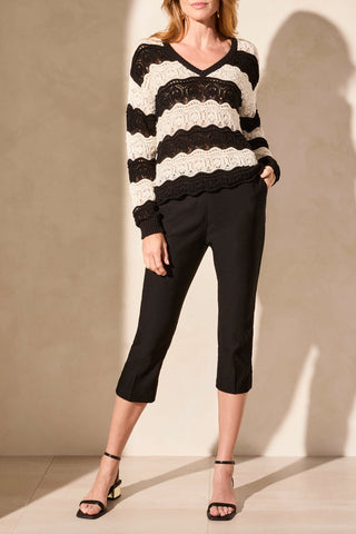 A woman wearing a long sleeve V-neck crochet swirl stripe sweater in black and cream.