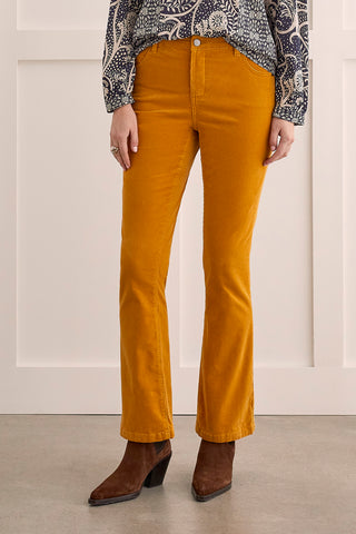 A model wearing suede pants in a marigold color paired with brown boots and a geometric top.