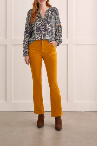 A model wearing suede pants in a marigold color paired with brown boots and a geometric top.