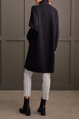 A woman wearing a black open-front coatigan with patch pockets over a white turtleneck sweater, paired with striped trousers.
