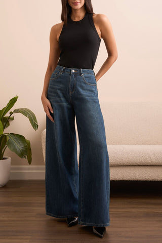 A woman wearing a black racer back tank top with a ribbed texture, paired with blue jeans.