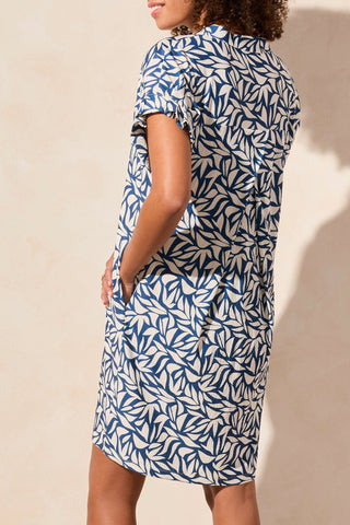 A model wearing a blue and white leaf patterned dress with rolled sleeves and a notch neckline.