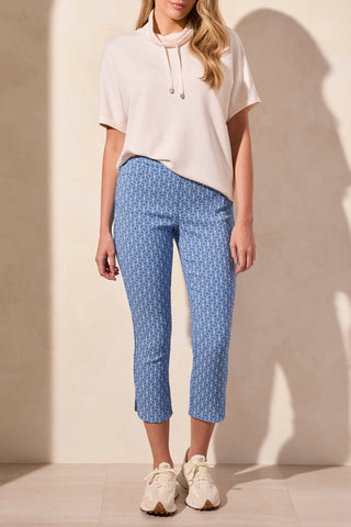A woman wearing a heathered oatmeal funnel neck top with a drawcord at the neckline, paired with blue patterned pants.