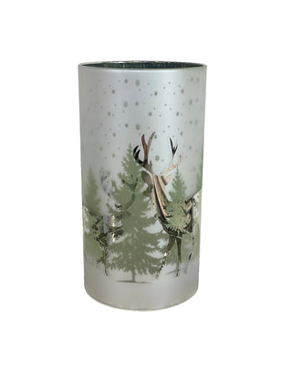 A frosted glass cylinder candle cover slip  featuring a printed winter forest design with green pine trees, deer, and falling snow.