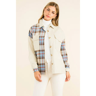 A woman modeling a long-sleeve button-front overshirt with a cream ribbed body and blue, brown, and tan plaid sleeves and chest panels, worn over a white turtleneck and white pants against a light beige studio background. THML Mixed Media Button Up Jacket