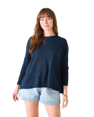 Woman wearing a navy sweater and light blue shorts on a white background. Mersea Catalina Cotton Crewneck Sweater in Navy