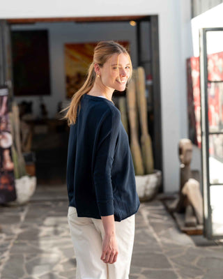 Woman standing in an art studio wearing a navy sweater and white pants. Mersea Catalina Cotton Crewneck Sweater in Navy