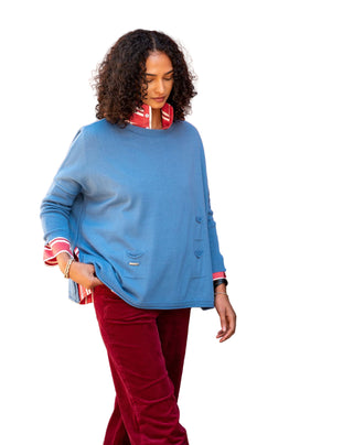 Woman wearing a blue sweater and red pants against an orange wall. Mersea Catalina Crewneck Sweater in Blue Dusk