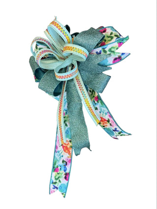 Spring & Teal Glitter Bow
A decorative bow made from layered ribbons, including a glittery sage green ribbon, a mint green ribbon with orange and yellow patterned edges, and floral patterned ribbons in pink, blue, and green, botanical watercolor braid