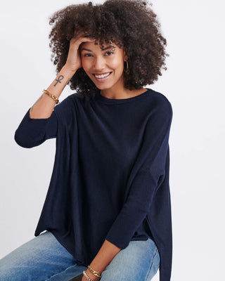 Woman wearing a navy blue sweater and jeans on a white background. Mersea Catalina Crewneck Sweater in Navy