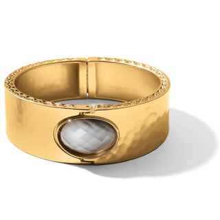 A gold-colored hinged bangle bracelet with a hand-set stone in the center, showcasing a textured surface with small gold accents along the rim. Brighton