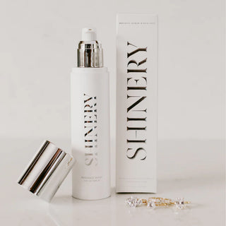 A bottle of Shinery Radiance Wash Jewelry Cleaner with its packaging box, alongside a piece of jewelry, against a white background.