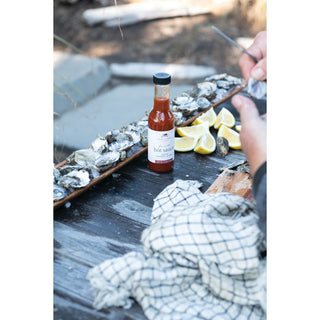 a photo of the finch and fennel fire roasted hot sauce sitting on a table by a plate of oysters with lemon. 